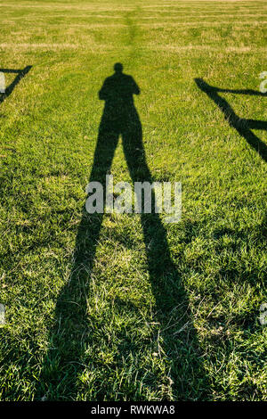 Ombre d'un homme se tenait dans une passerelle, rétroéclairé par le soleil. Son ombre s'étend dans le champ d'herbe et au-delà de la piste Banque D'Images