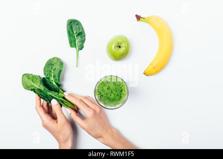 Top View woman's hands holding bunch of spinach près de pomme, banane et verre avec boisson smoothie vert sur fond blanc, télévision lay. Banque D'Images