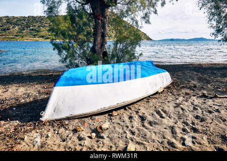 Blanc bleu vintage bateau en bois rustique à l'envers sur une plage de sable en face de la mer et l'arrière-plan de l'île Banque D'Images