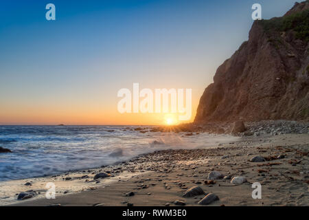 Belle vue de la côte de plage comme les vagues sur le rivage, de hautes falaises en arrière-plan, et le soleil à l'horizon au crépuscule, Dana Point, fabriquées main e Banque D'Images