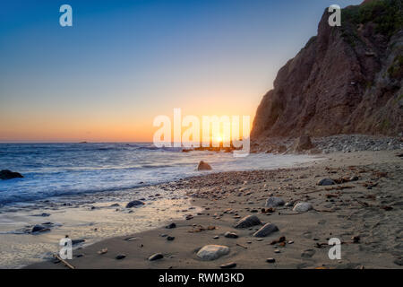 Belle vue de la côte de plage comme les vagues sur le rivage, de hautes falaises en arrière-plan, et le soleil à l'horizon au crépuscule, Dana Point, fabriquées main e Banque D'Images