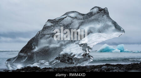 Morceau de glace sur la plage du Diamant, près de Jokusarlon, avec l'océan derrière elle le long de la côte sud de l'Islande, Islande Banque D'Images