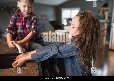 Tout-petit aider sœur se laver les mains dans un évier de cuisine Banque D'Images