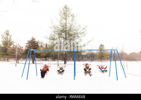 L'homme et des enfants se balançant sur ligne de jeux pour enfants balançoires dans la neige Banque D'Images