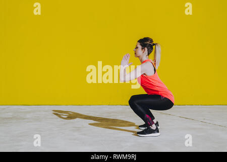 Jeune femme en faisant des exercices de sport équipe près de mur jaune Banque D'Images