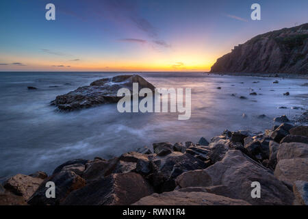 Une longue exposition photo de substitution, de hautes falaises et les vagues s'écraser dans un grand rock formation après le coucher du soleil, Dana Point, Californie Banque D'Images