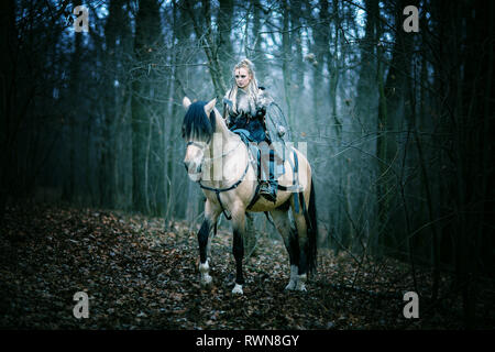 Femme guerrière sur un cheval dans les bois. Viking scandinave cheval de la hache à la main, cheveux blonds en vêtements traditionnels à col fourré, mak guerre Banque D'Images