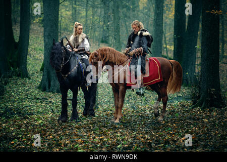 Un homme sur femme guerriers chevaux dans les bois. Les vikings scandinaves équitation avec des haches dans les mains. Vêtements traditionnels à col fourré. Reconstructio Banque D'Images