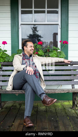 Un homme est assis sur un banc à l'extérieur d'un bâtiment et de rires qu'il regarde ailleurs, Fort Langley, Colombie-Britannique, Canada Banque D'Images