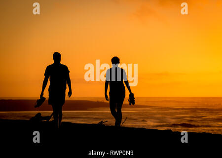 Coucher du soleil sur la plage de Hokitika, avec deux jeunes touristes marchant sur la plage Banque D'Images
