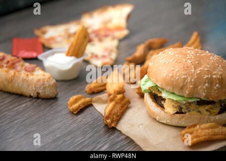 Le fast food. Hamburger, frites deluxe, pizza, fromage, laitue et sauce à la crème aigre. Banque D'Images