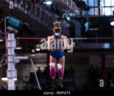 Une athlète féminine de tomber dans l'air après le dégagement d'une hauteur d'une compétition de saut à la perche, de l'arrière. Banque D'Images