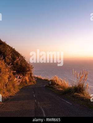 Big Sur, Californie - route sinueuse mène les collines côtières vers l'océan Pacifique et l'horizon au coucher du soleil. Banque D'Images