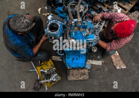 Travail mécanique auto colombien sur un moteur de camion en face d'un atelier de réparation de voiture dans le Barrio Triste, Medellín, Colombie. Banque D'Images