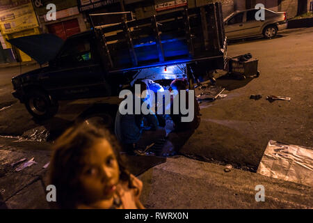 Travail mécanique auto colombien sur un essieu arrière d'une camionnette pendant la nuit dans le Barrio Triste, Medellín, Colombie. Banque D'Images