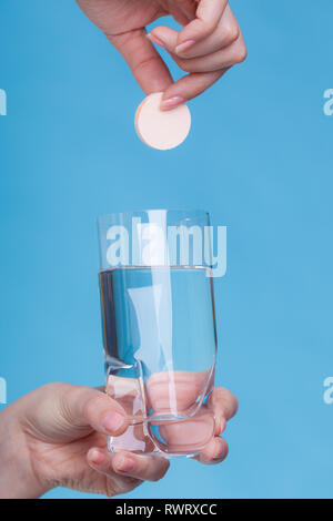 Des vitamines, de la santé, des médicaments. Personne jeter le supplément minéral de vitamine comprimé effervescent dans un verre d'eau. Studio shot sur fond bleu Banque D'Images