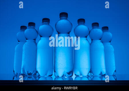 Image aux couleurs de bouteilles en plastique avec de l'eau dans la rangée sur fond bleu néon Banque D'Images