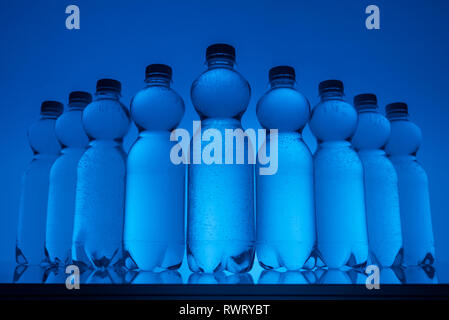 Image aux couleurs de bouteilles en plastique transparent avec de l'eau sur fond bleu néon Banque D'Images