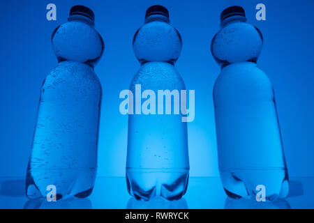 Image aux couleurs de bouteilles en plastique transparent avec de l'eau sur fond bleu néon Banque D'Images