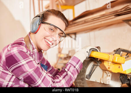 Jeune femme en tant que menuisier stagiaire avec des lunettes et des protections pour les oreilles à la vu chop Banque D'Images