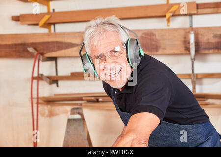 Smiling Carpenter. Master avec protection auditive travaille sur la scie circulaire à l'atelier Banque D'Images