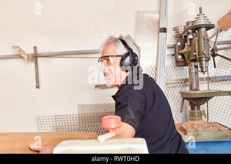 Carpenter senior avec protection auditive fonctionne avec du bois dans la menuiserie ou grumes Banque D'Images