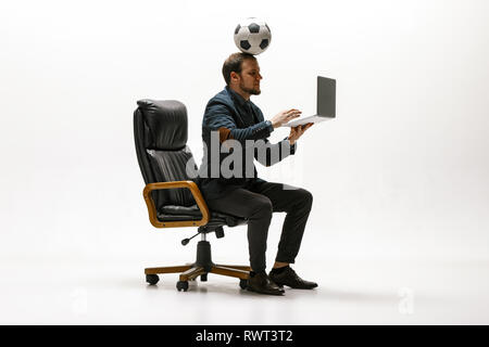 Businessman with foot ball in office. Soccer freestyle. Concept de l'équilibre et l'agilité de l'entreprise. Manager trucs et astuces portez assis sur une chaise et de travail sur ordinateur portable isolé sur fond blanc studio. Banque D'Images