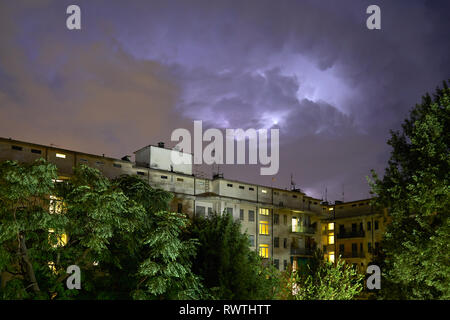 Les bâtiments et les arbres verts dans la nuit, illuminé le ciel pendant un orage en Italie Banque D'Images