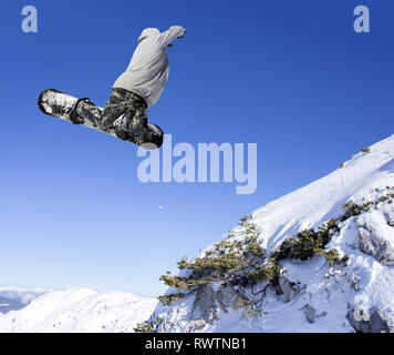Snowboarder jump saut extrême au-dessus les montagnes en journée ensoleillée Banque D'Images