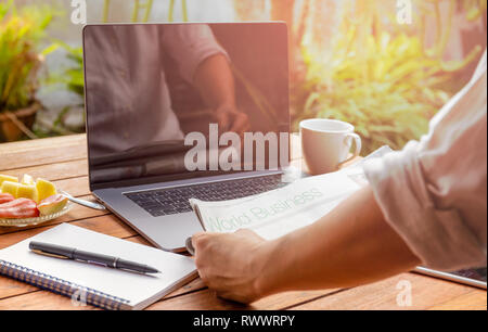Businessman reading newspaper avec ordinateur portable et ordinateur portable sur la table. Banque D'Images