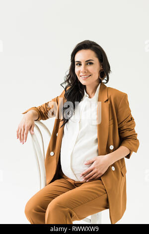 Smiling brunette pregnant woman sitting on chair isolated on white Banque D'Images