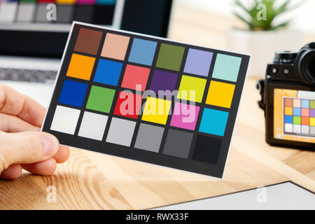 L'homme est titulaire d'une carte en papier avec des couleurs d'essai pour la gestion des couleurs et le profilage. L'équipement pour ajuster et équilibrer photographie. Appareil photo et ordinateur portable sur backgrou Banque D'Images