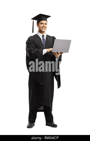 Portrait d'un jeune homme d'une graduation gown noire et les titulaires d'un ordinateur portable et smiling at the camera isolated on white backgroun Banque D'Images