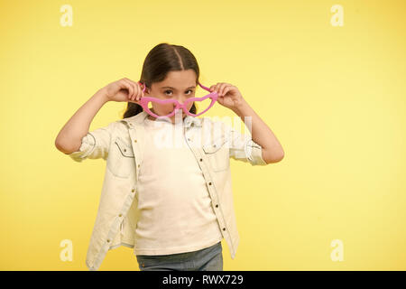 Fille look dans des verres en forme de coeur sur fond jaune. Petit enfant avec accessoire de mode. Restez calme et porter des lunettes cool. Beauté Funky style. Valentines Day. Banque D'Images