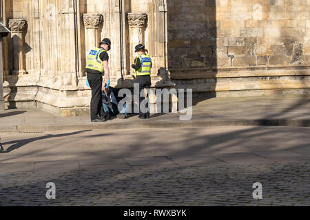 Deux agents de police fréquentant un homme se sont assis sur un trottoir à côté de York Minster, York, North Yorkshire, Angleterre, Royaume-Uni. Banque D'Images