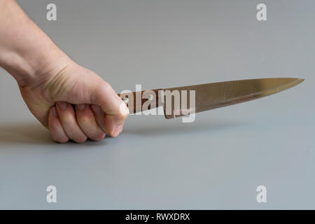 La main de l'homme avec un couteau sur fond gris. Concept de la violence. Banque D'Images