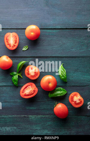 Une photo prise à la verticale de tomates heirloom organiques avec des feuilles de basilic sur un fond rustique foncé with copy space Banque D'Images