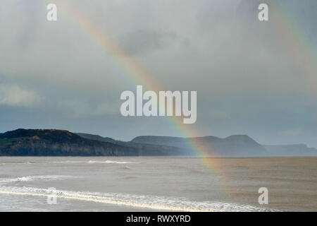 Lyme Regis, dans le Dorset, UK. 7 mars 2019. Météo britannique. Un arc-en-ciel à la ville balnéaire de Lyme Regis dans le Dorset à la recherche vers les falaises de Stonebarrow Hill et Golden Cap sur un après-midi de soleil et d'une douche. Crédit photo : Graham Hunt/Alamy Live News Banque D'Images