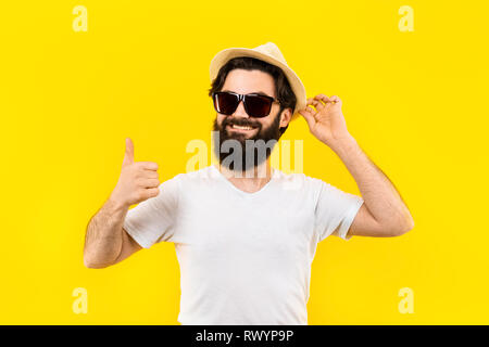 Studio portrait d'un barbu dans un t-shirt et lunettes de soleil et le panama sourit et montre un concept, comme de l'humeur de plage en été Banque D'Images