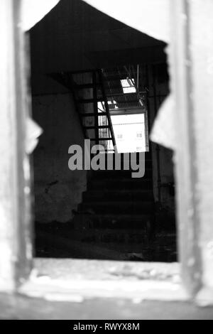 À travers une fenêtre cassée dans un bâtiment abandonné en noir et blanc. Banque D'Images