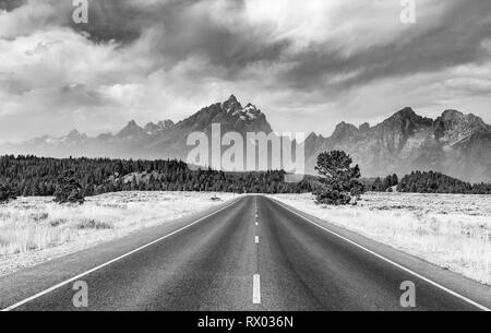 Noir et blanc, route de campagne en face de montagnes escarpées avec ciel nuageux, plage de Grand Teton, Grand Teton National Park Banque D'Images