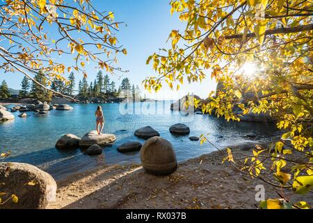 Young woman in bikini debout sur une pierre ronde dans l'eau, Bay au lac Lake Tahoe, parc d'État Sand Harbor, Port, Californie Banque D'Images
