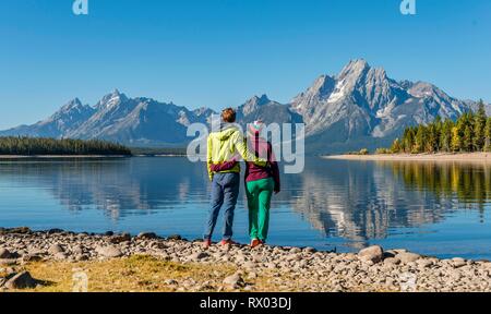 Jeune femme et jeune homme debout côte à côte sur la rive, à la recherche dans le paysage, les montagnes reflété dans le lac Banque D'Images