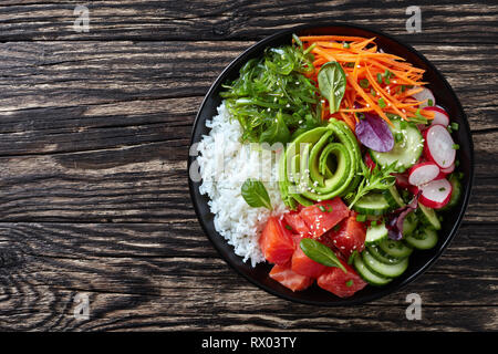 Ahi Poke saumon biologiques crus bol avec du riz, des algues, de l'avocat rose, radis, carotte, concombre et salade verte, parsemée de petits oignons et le sésame se Banque D'Images