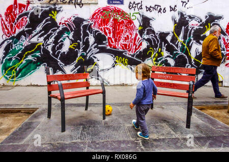 Vue sur la rue, UN enfant jouant avec un ballon et un homme passant autour du mur de graffiti coloré, Valence, rue de la vieille ville quartier El Carmen Banque D'Images