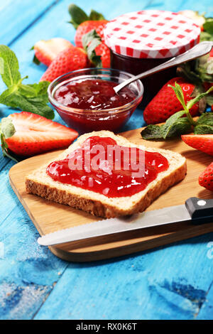 Griller le pain avec de la confiture de fraise ou de la marmelade sur table bleu rustique servi avec du beurre pour le petit déjeuner ou le brunch Banque D'Images