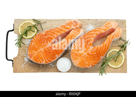 Deux darnes de saumon cru avec les tranches de citron, le sel et le romarin sur une planche à découper. Vue de dessus, isolé sur blanc. Banque D'Images