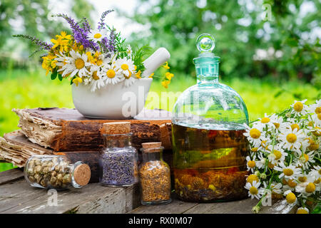 Herbes de guérison de mortier, des bouteilles d'huile essentielle en santé ou de l'infusion et sécher les herbes médicinales, les vieux livres et bouquet de fleur de camomille. Phytothérapie Banque D'Images