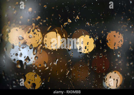 Un plan macro de gouttes sur les vitres pendant la pluie de nuit dans la ville. Bokeh colorées en arrière-plan Banque D'Images