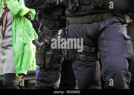 Détails de la trousse de sécurité de deux agents de la police anti-émeute (y compris des menottes, 9mm pistolet, station de radio et baton) assis parmi les civils Banque D'Images